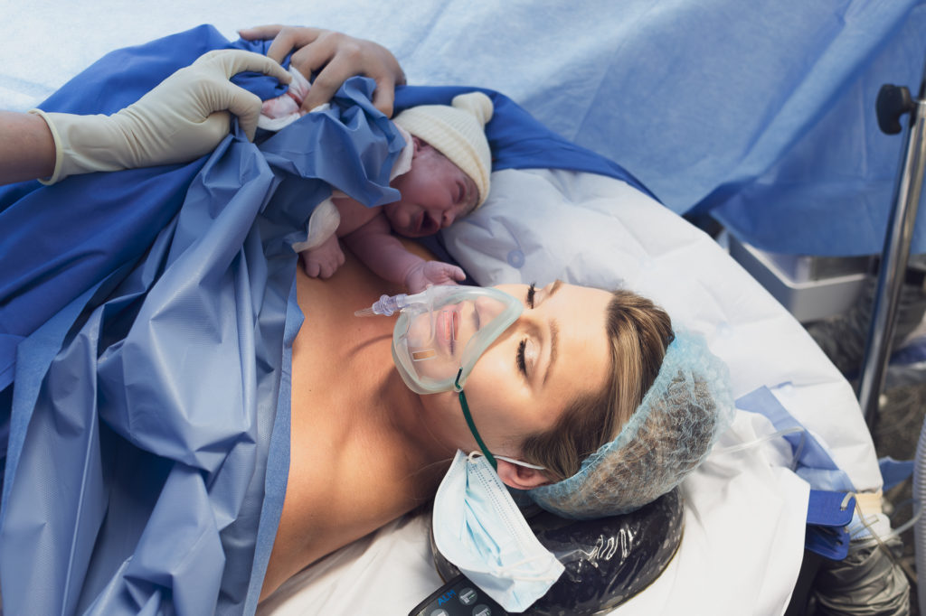 Femme avec un masque sur le visage qui tient son bebe apres l'accouchement