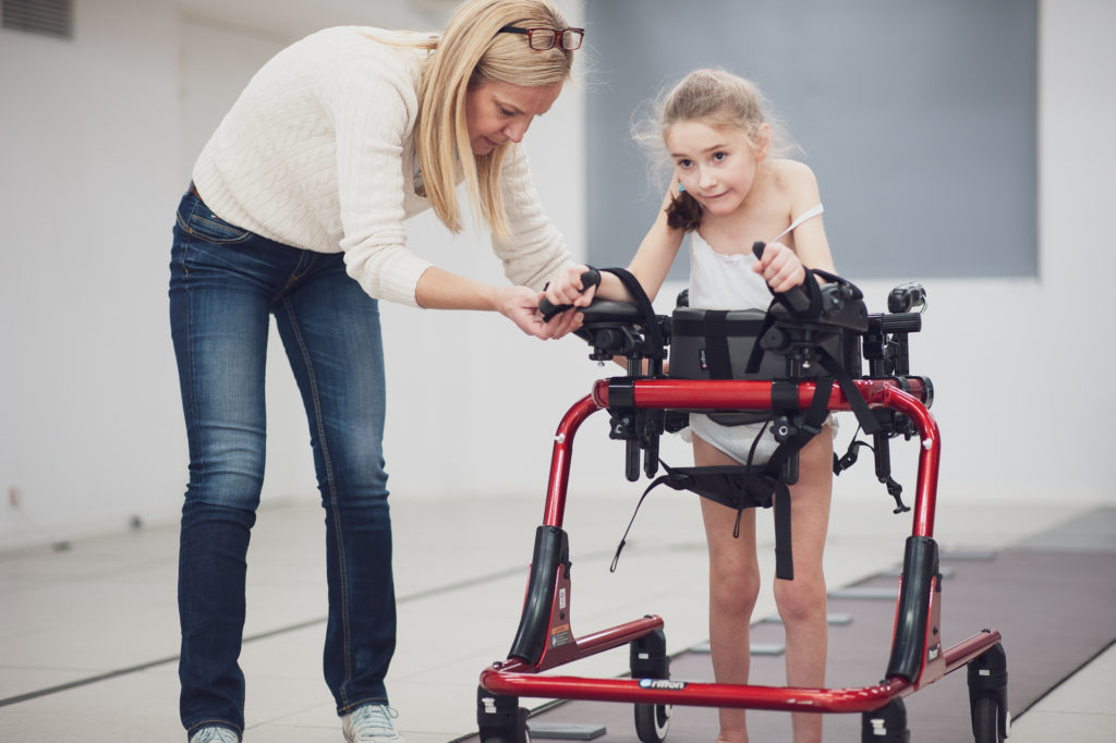 Enfant handicapee tenant son deambulateur pendant un exercice et aidee par une kinesitherapeute