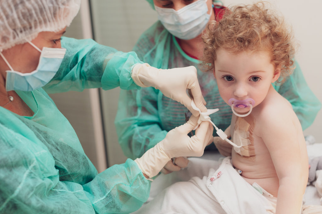 Enfant avec sa tetine dont la maman habillee en sterile change le catetere 