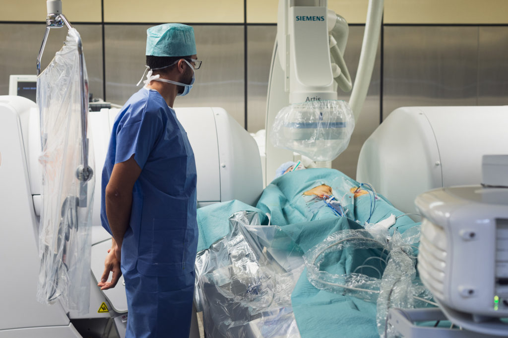 Medecin habille en bleu  regardant le patient pris entre les aimants pendant une operation du coeur